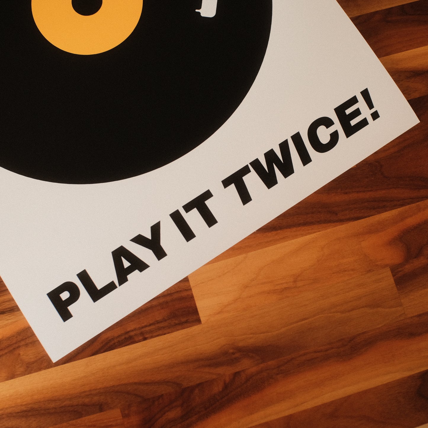 Typography music poster featuring a bold black vinyl record design with a yellow label, accompanied by the phrase 'IF IT'S NICE... PLAY IT TWICE!' in striking black font. Midcentury modern themed wall art.